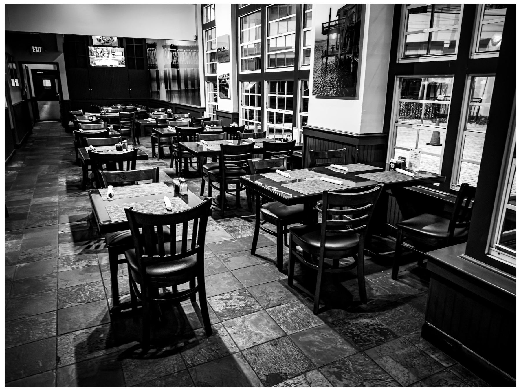 A black and white photograph depicts an empty restaurant with neatly arranged tables and chairs.