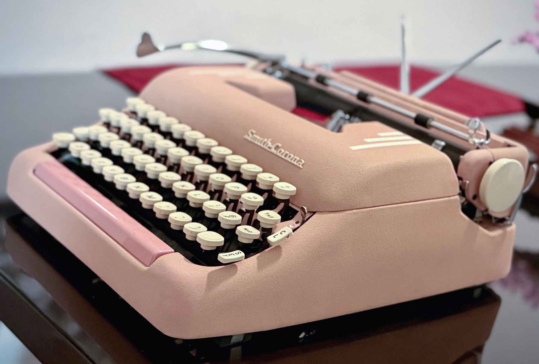 Auto-generated description: A vintage pink Smith-Corona typewriter sits on a reflective dark surface.